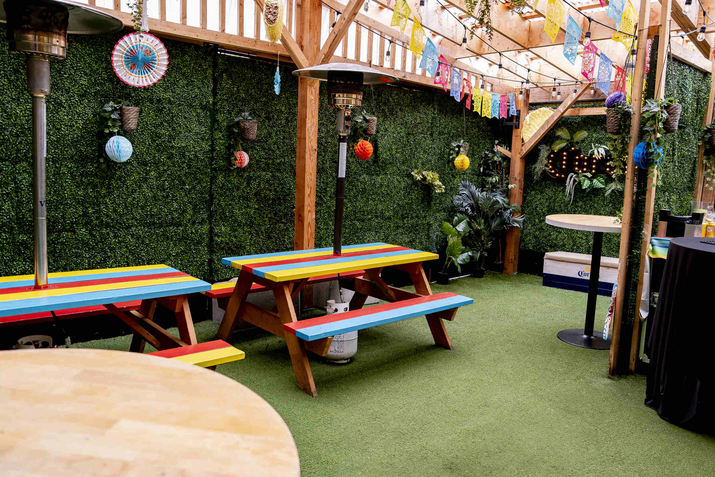 The Pawn Shop YVR's lively Hideaway back patio event space, downtown Vancouver. Colourful flags, string lights under a pergola, and red, yellow, blue picnic tables.