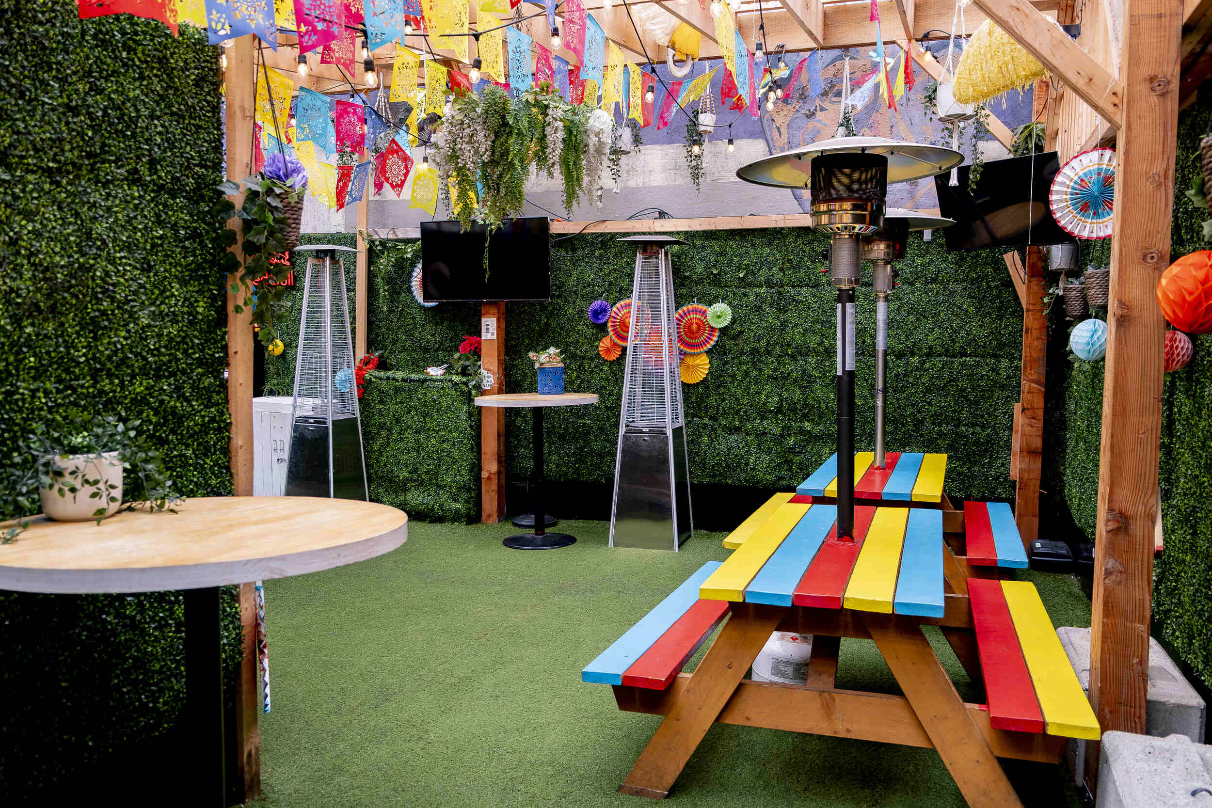 Close-up of a vibrant red, yellow, blue picnic table at The Pawn Shop YVR's Hideaway patio. Patio heater and fan decorations visible