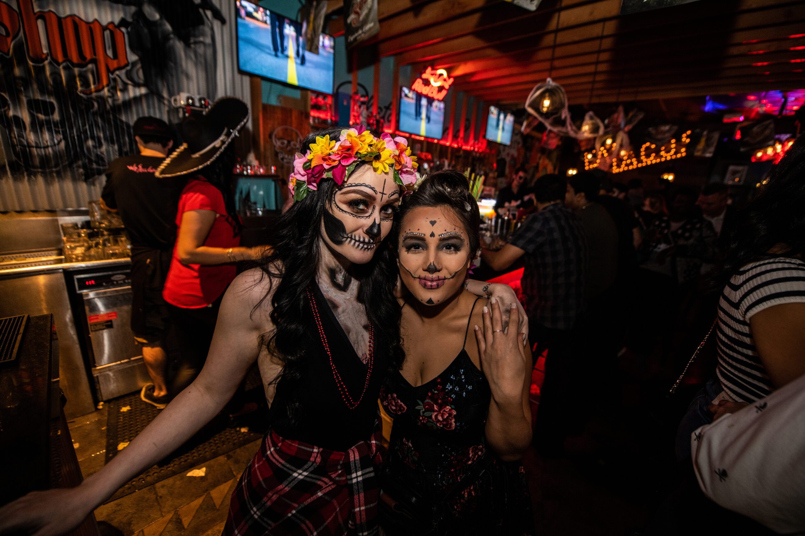 Two happy guests in Day of the Dead (Día de los Muertos) makeup posing inside the brightly lit tequila and taco bar.