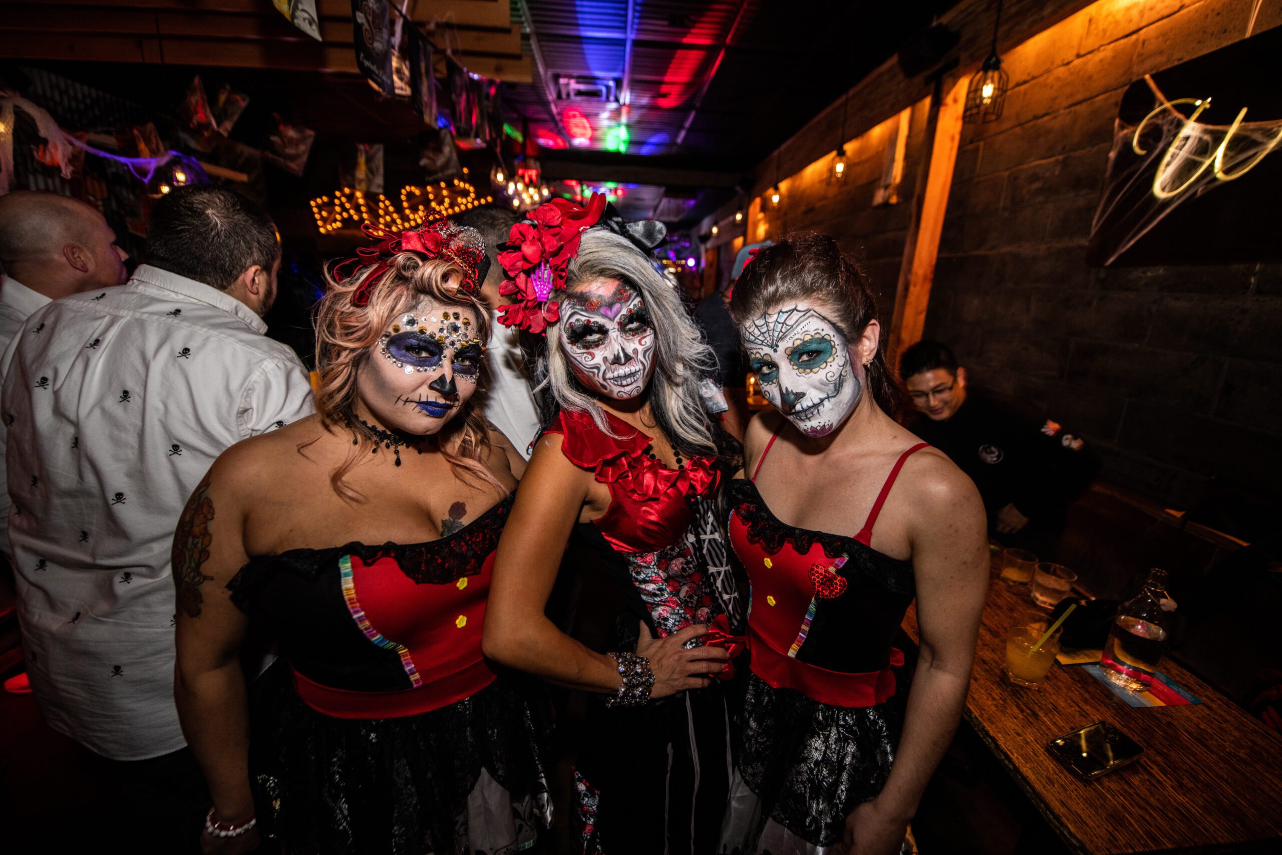 Three guests in elaborate Day of the Dead costumes and face paint enjoying the vibrant, low-lit restaurant vibes at the Pawn Shop YVR.